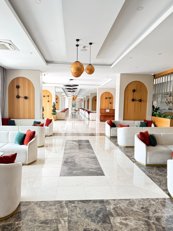 Long, Bright Hallway In A Commercial Space Featuring White Seating Areas And Architectural Wooden Arch Details.